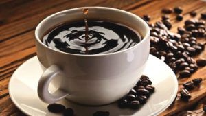 kopje zwarte koffie naast koffiebonen op houten tafel