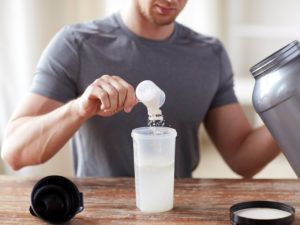 Man doet een scoop met eiwit poeder in een drinkbeker