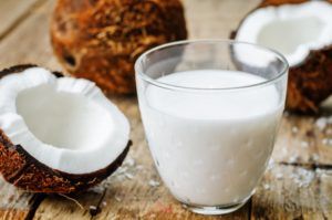 glas kokosmelk naast opengebroken kokosnoot op houten tafel