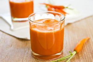Wortelen en sinaasappelsap in een glas op houten tafel